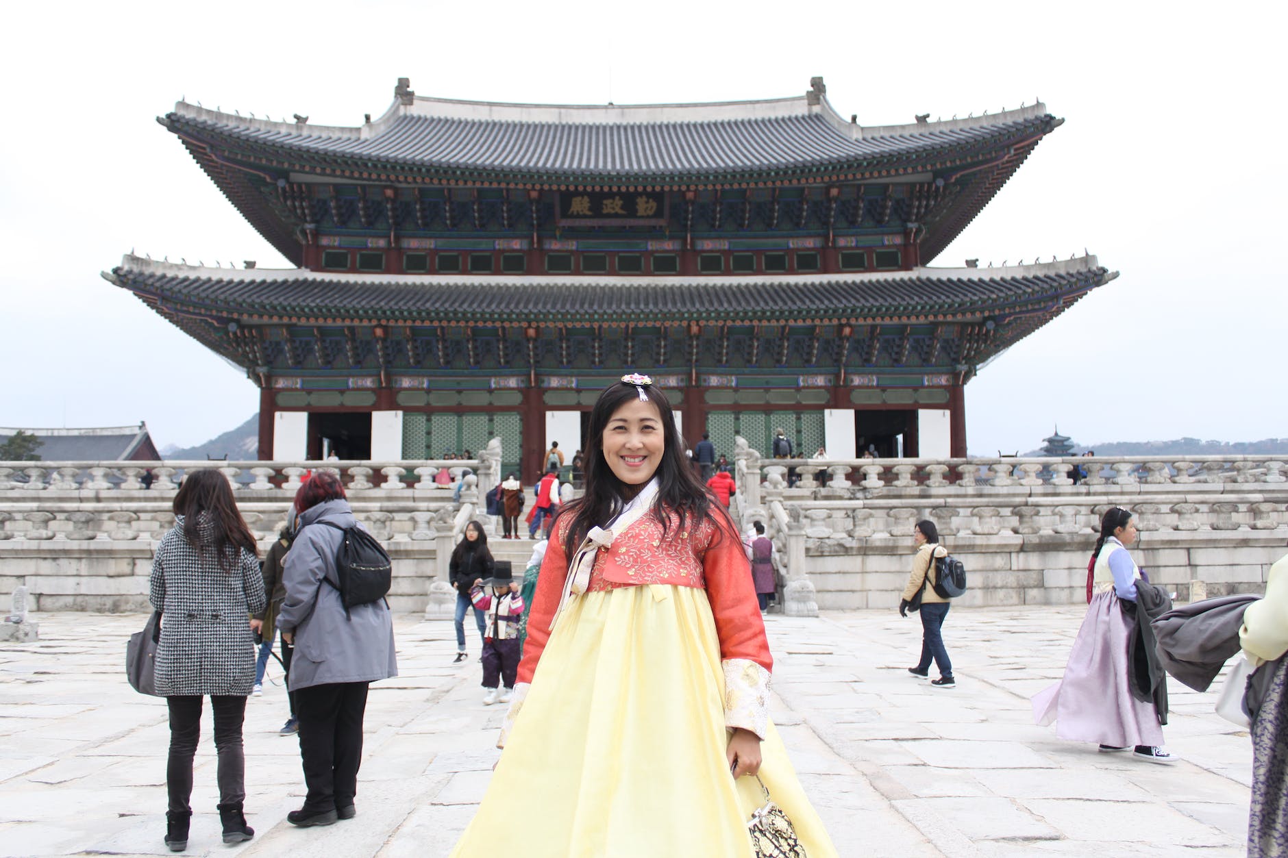 cheerful woman standing against pagoda in cloudy weather